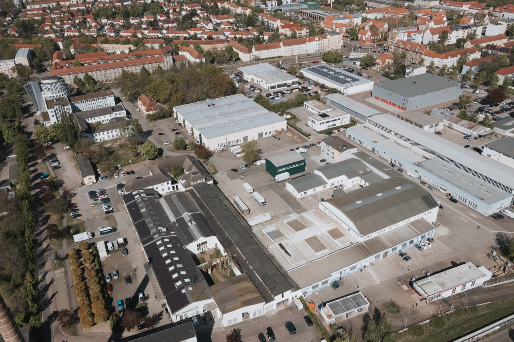 Luftaufnahme des Gewerbeparks mit Hallen und Bürogebäuden, dahinter Wohnbebauung