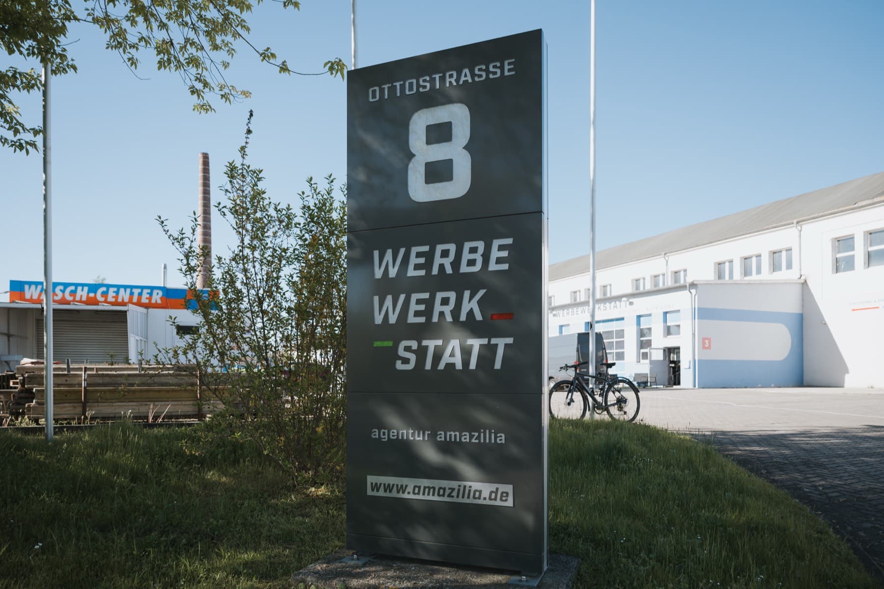 Adress-Pylon Ottostraße 8 an der Einfahrt zum 1A Gewerbepark, im Hintergrund Werkstatthalle und Waschanlage