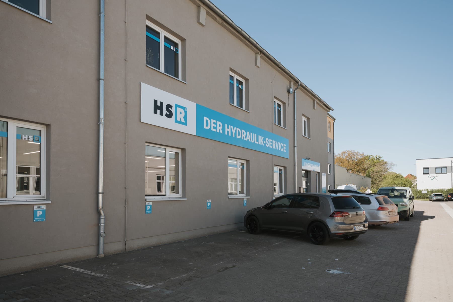 Fassade von Gebäude 6 mit Firmenschild des Hydraulik-Service und Kundenparkplätzen