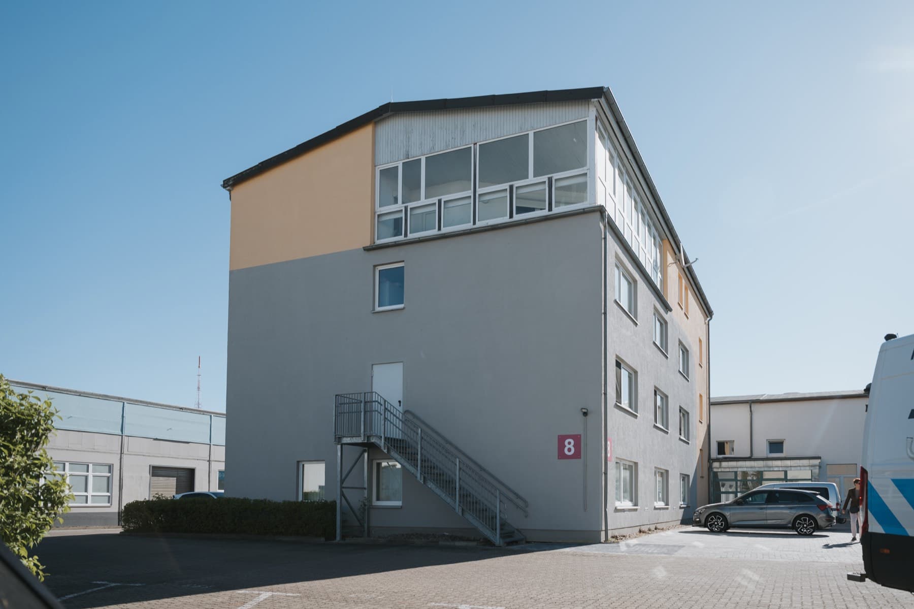 Bürogebäude 8 mit verglastem Dachgeschoss und Parkplätzen, Außenansicht bei blauem Himmel