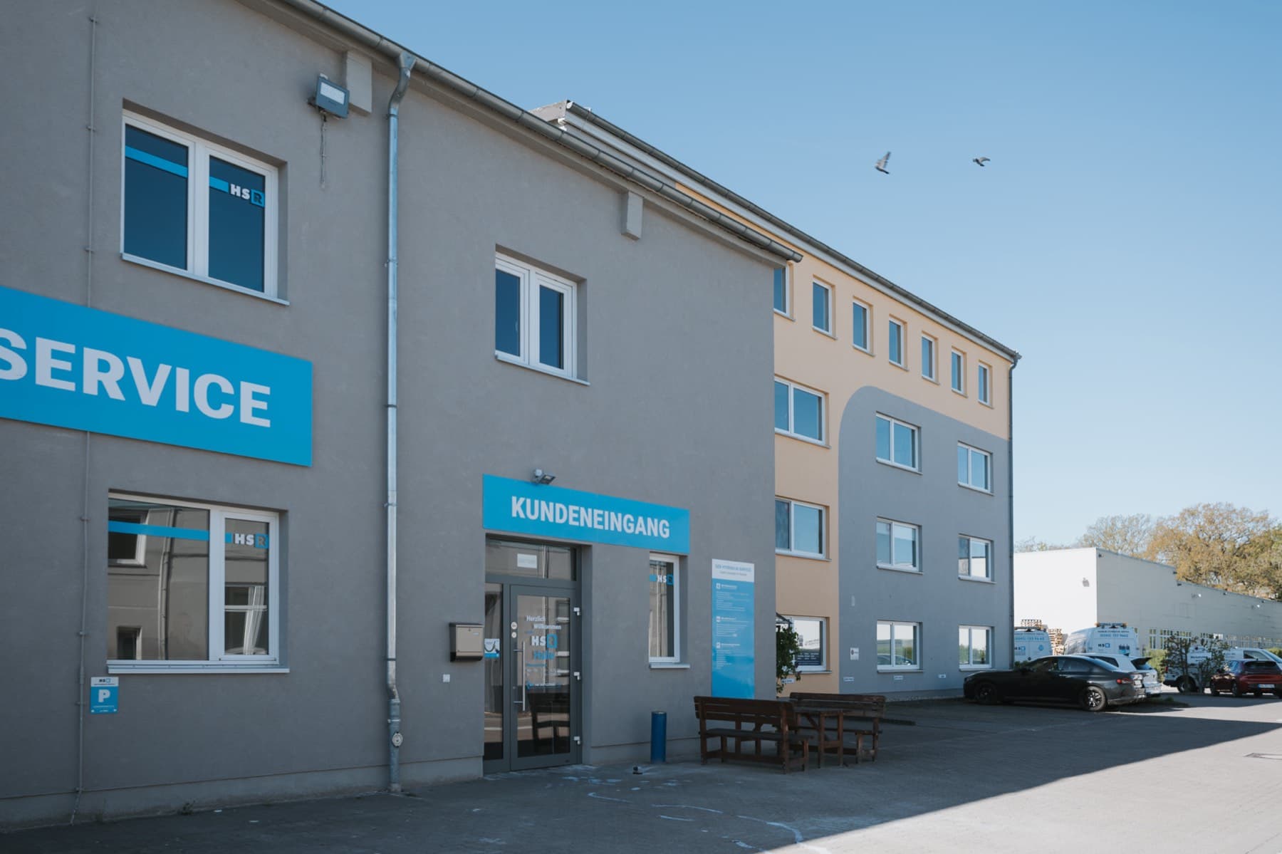 Kundeneingang mit Sitzgruppe am Gebäude 8, dahinter das Bürohaus in Orange-Grau
