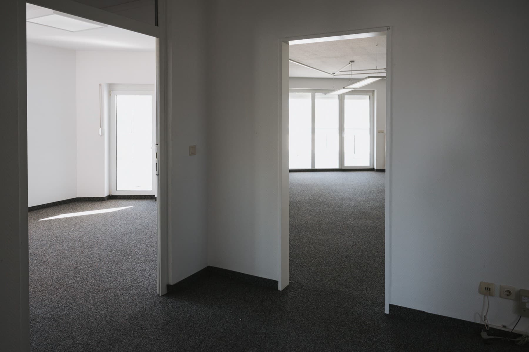 Zwei helle Büroräume mit Deckenleuchten und bodentiefen Fenstern im Gebäude 8