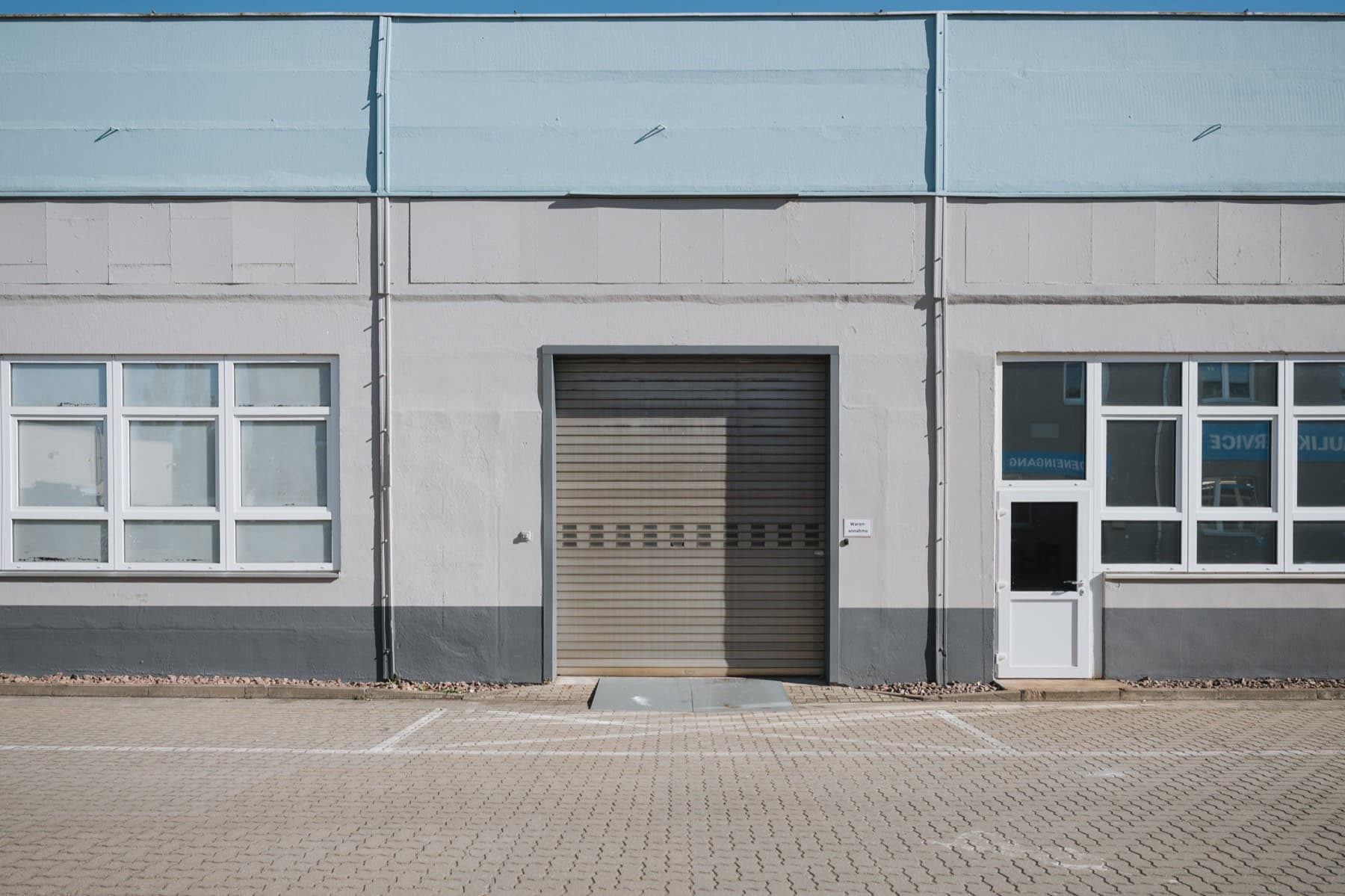 Halle 1 — Fassade mit Rolltor der Warenannahme, weißer Nebeneingangstür und Fensterbändern