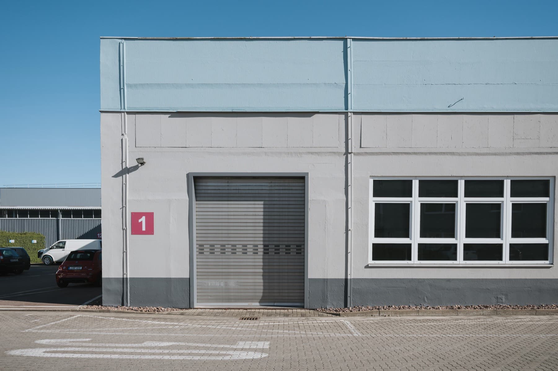 Halle 1 — Gebäudeecke mit Rolltor, Hallennummer 1 und großem Sprossenfenster