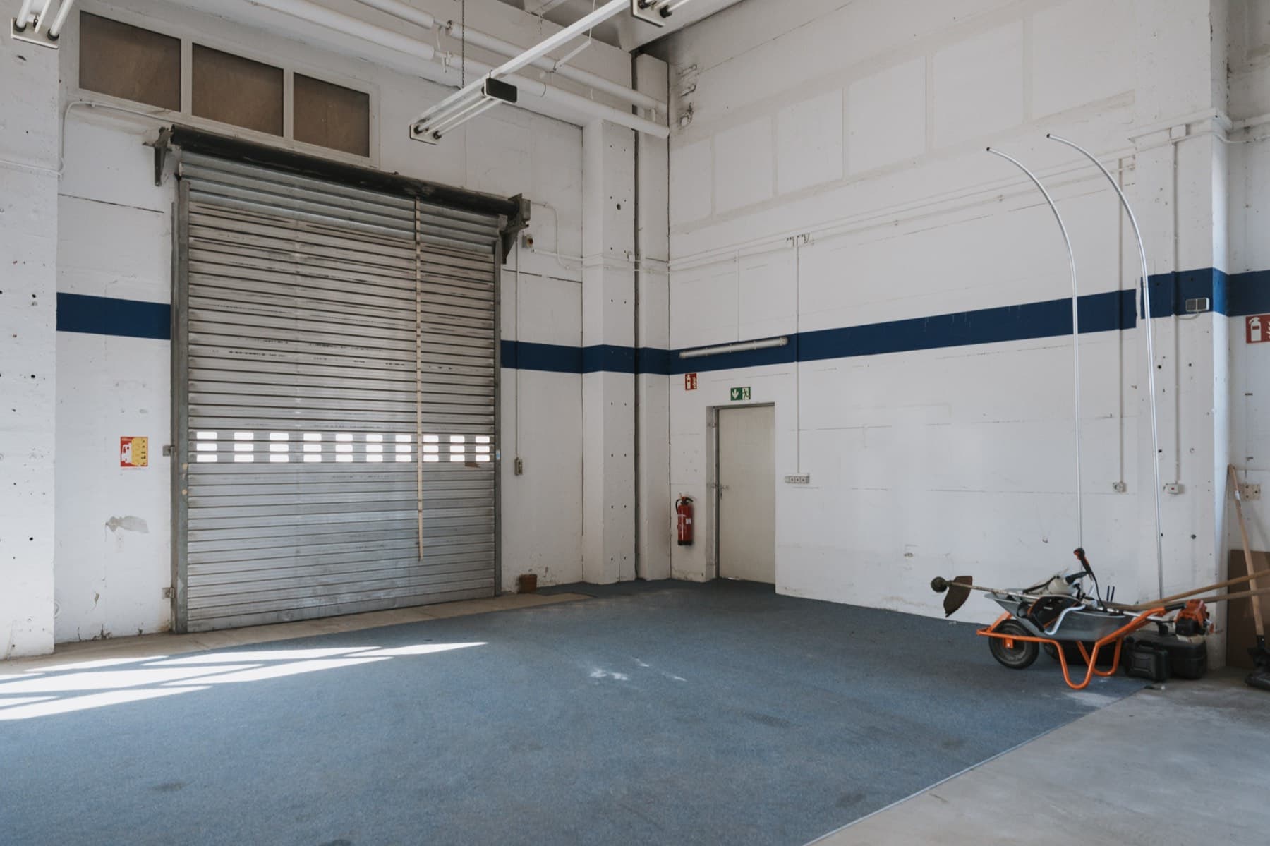 Halle 1 — Innenraum mit Rolltor, blauem Wandstreifen und blauer Bodenfläche
