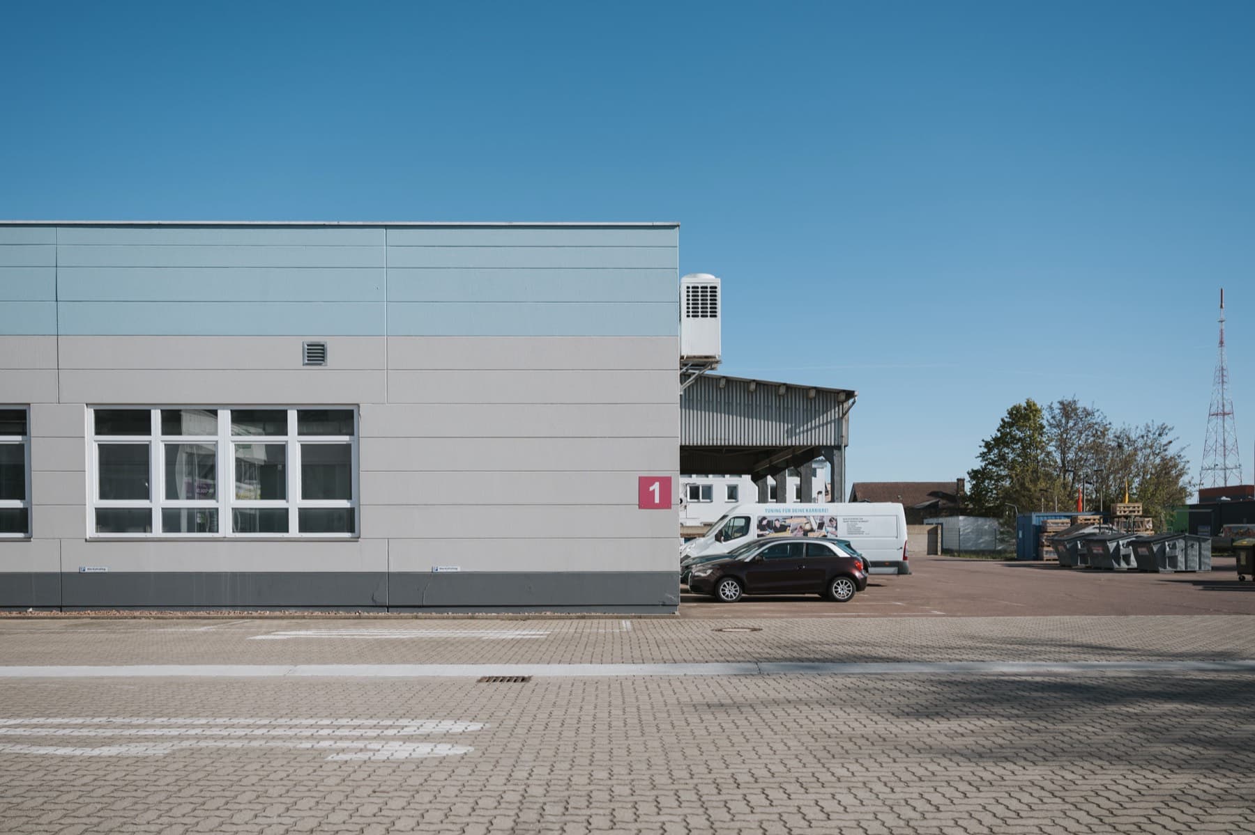 Halle 1 — Gebäudekante mit Hallennummer 1, dahinter Hof mit Lagerfläche und überdachtem Vordach