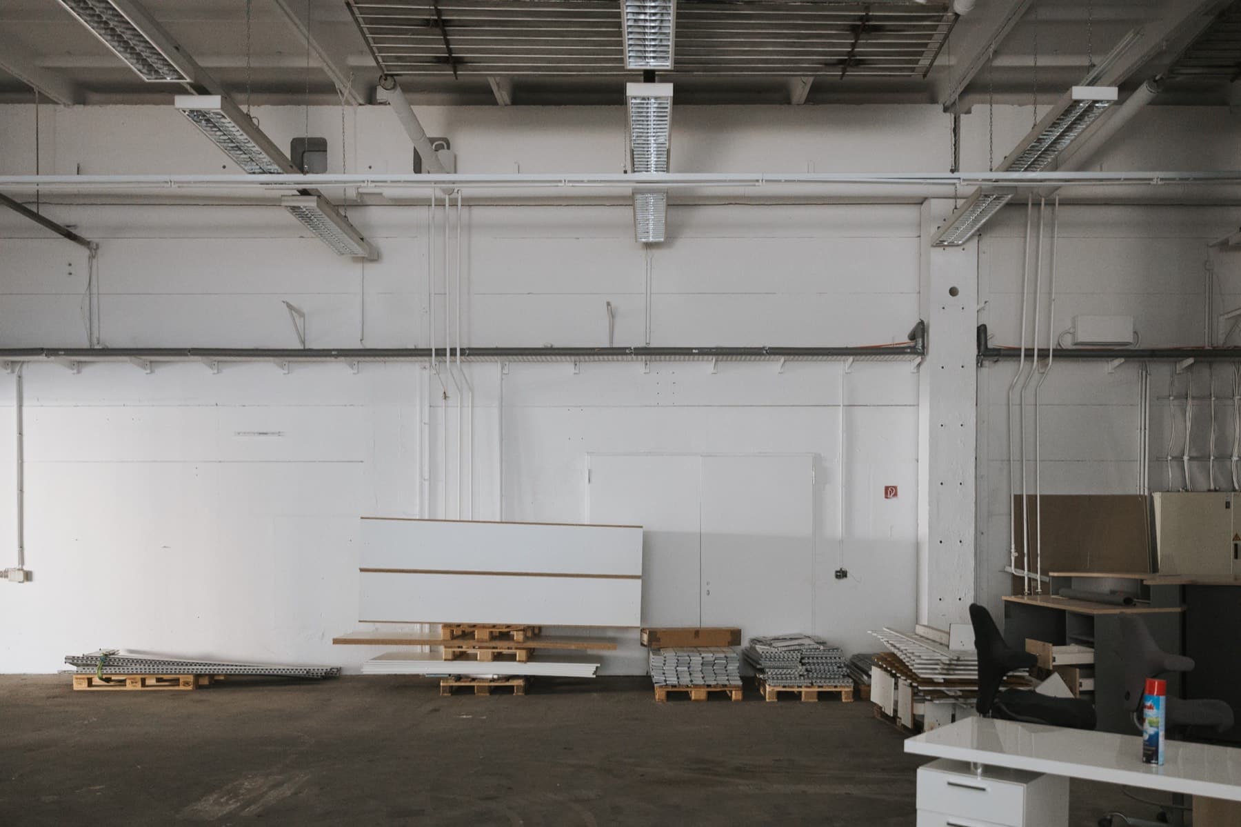 Halle 1 — Lagerbereich mit Paletten und Plattenmaterial an der Wand, Doppeltür im Hintergrund