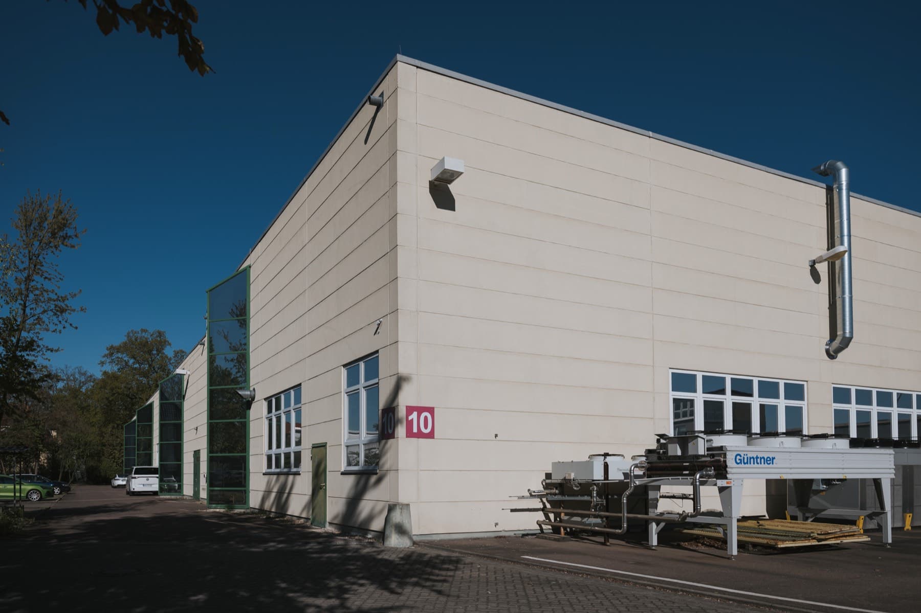 Gebäudeecke der Halle 10 mit Hallennummer, grün gerahmten Glasgiebeln und Kühltechnik