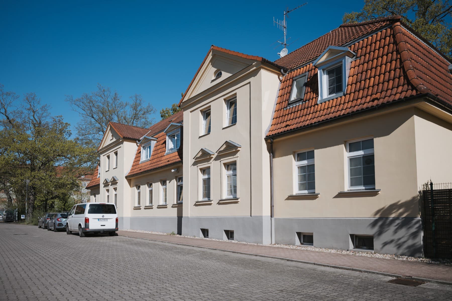 Halle 11 — Außenansicht des sanierten Altbaus mit Ziegeldach, Zwerchgiebeln und gepflasterter Straße