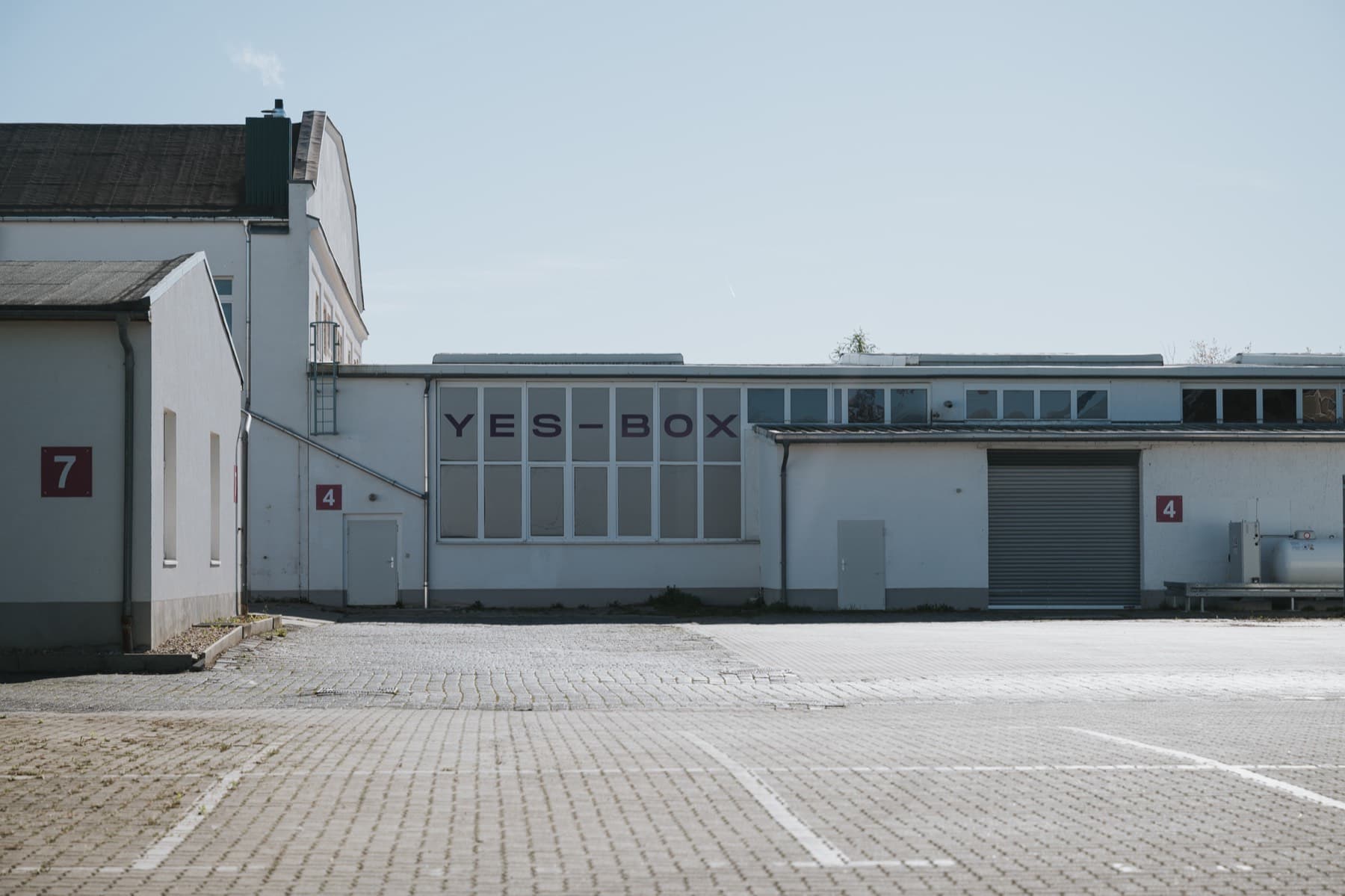 Halle 4 mit YES-BOX-Schriftzug und roten Hallenschildern, davor Parkplätze im Gewerbepark