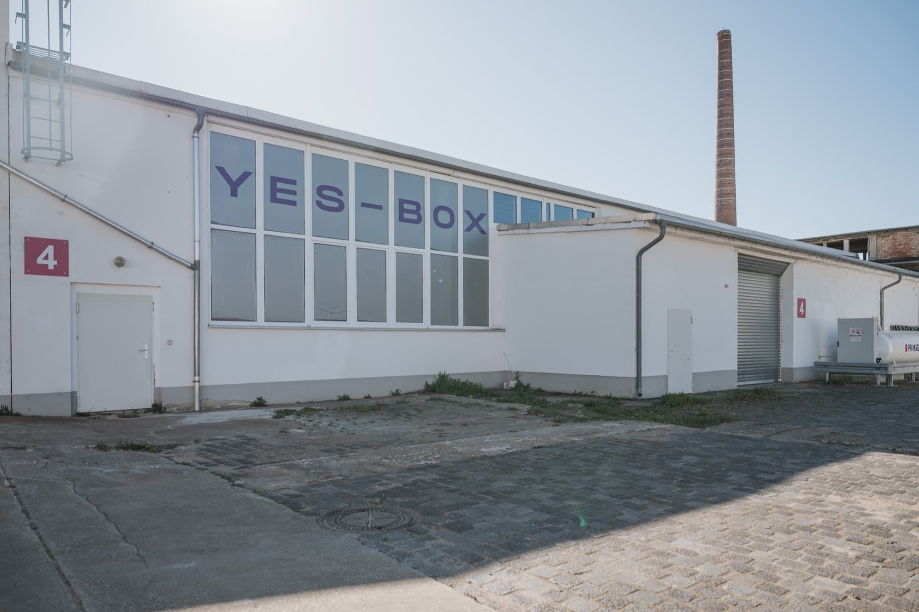 YES-BOX-Fensterband der Halle 4, dahinter der Backstein-Schornstein