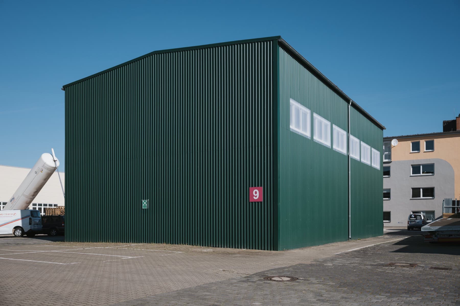 Halle 9 — Außenansicht der grünen Stahlhalle mit Giebel, Fensterband und Hallennummer 9